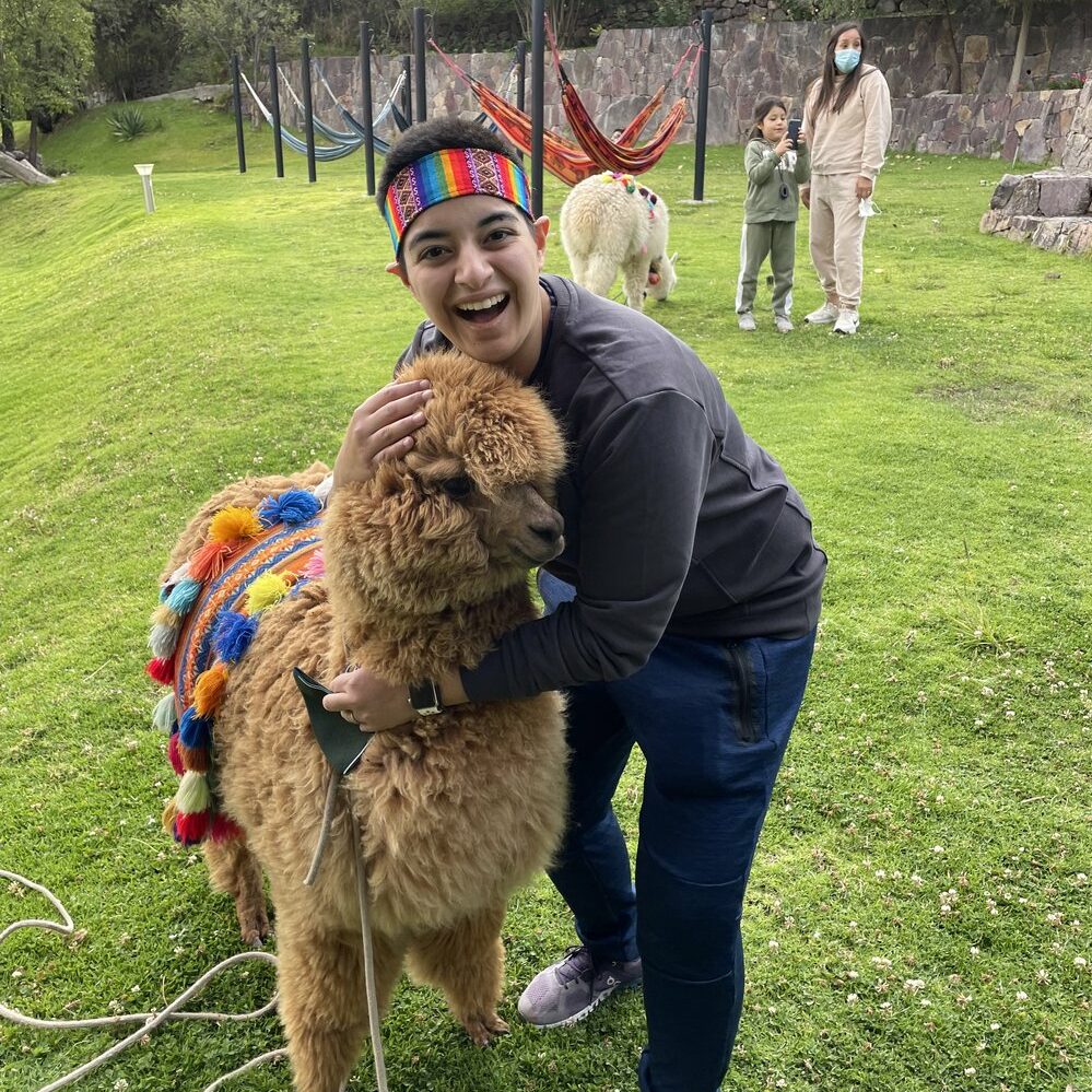 Sarah Malhotra wears a colorful headband and poses with an alpaca