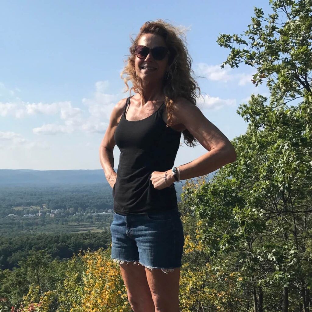 Mary Liz Licata stands outside on a hill, a view of valley behind her